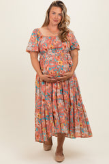 woman wearing a floral pattern pink maternity dress, holding her baby bump with a smile