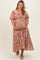 woman wearing a floral pattern pink maternity dress, holding her baby bump with a smile