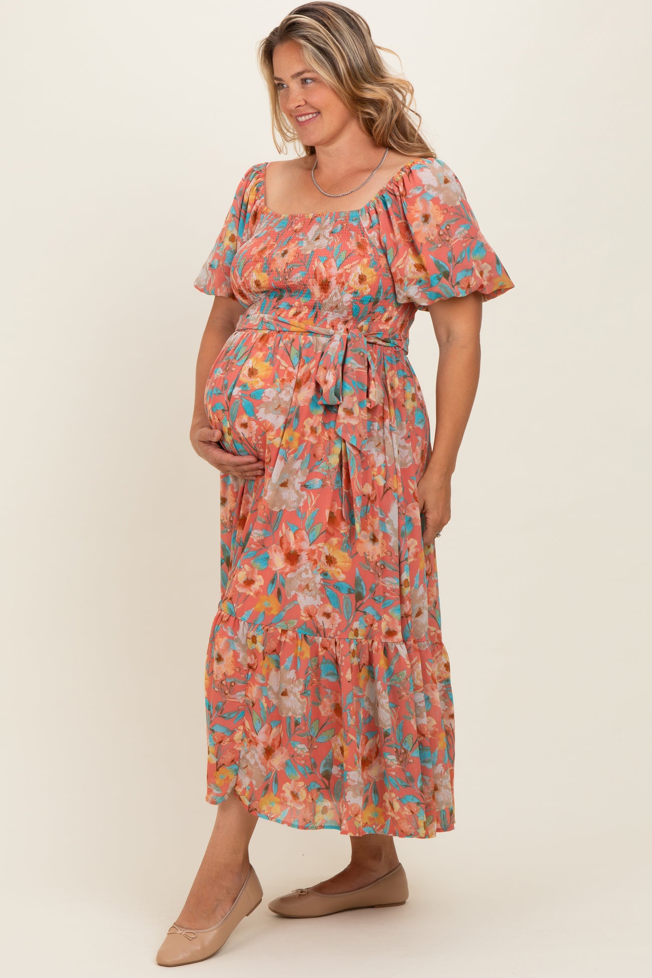 woman wearing a floral maternity dress with short sleeves and a tie waist, showcasing her baby bump