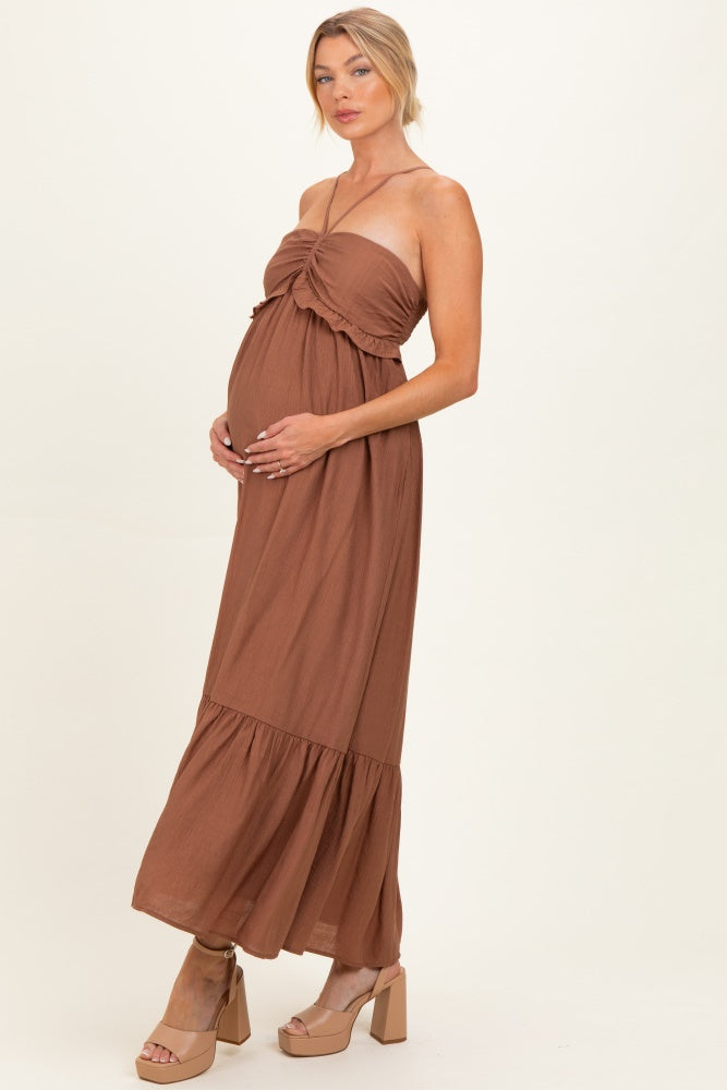 woman wearing a brown strapless maternity maxi dress with a tie detail and tiered hem, holding her baby bump