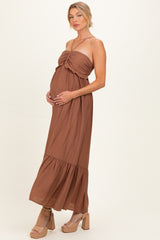 woman wearing a brown strapless maternity maxi dress with a tie detail and tiered hem, holding her baby bump