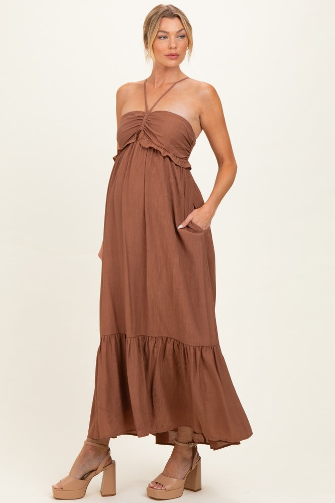 woman wearing a brown maternity maxi dress with a halter neck and ruffle details, showcasing her baby bump
