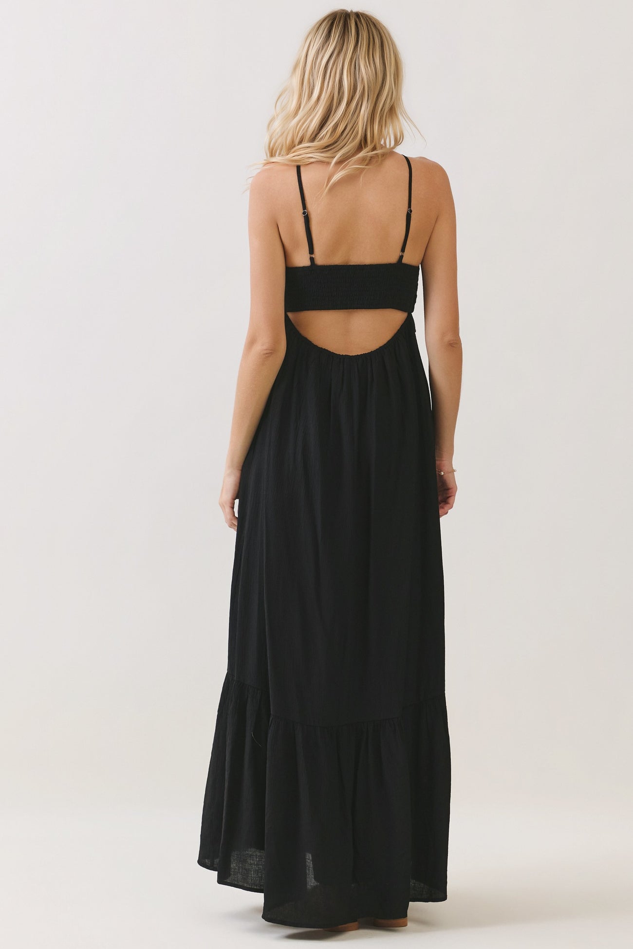 woman wearing a black maxi dress with a back cutout and tiered hemline