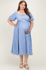 woman wearing a blue floral maternity dress with puff sleeves and a fitted waist, holding her baby bump
