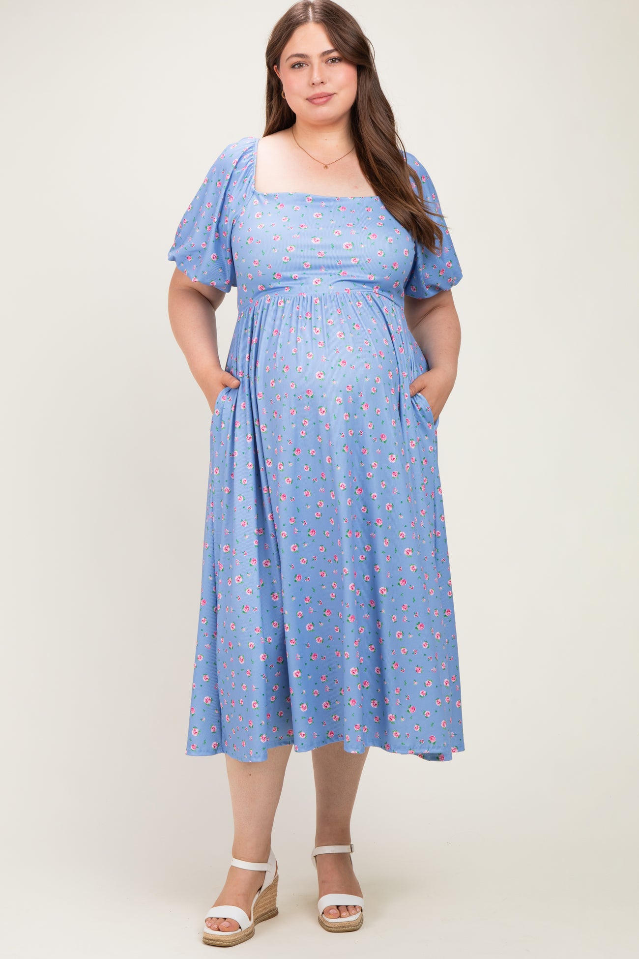 woman wearing a light blue floral maternity dress with puff sleeves and pockets, showcasing her baby bump