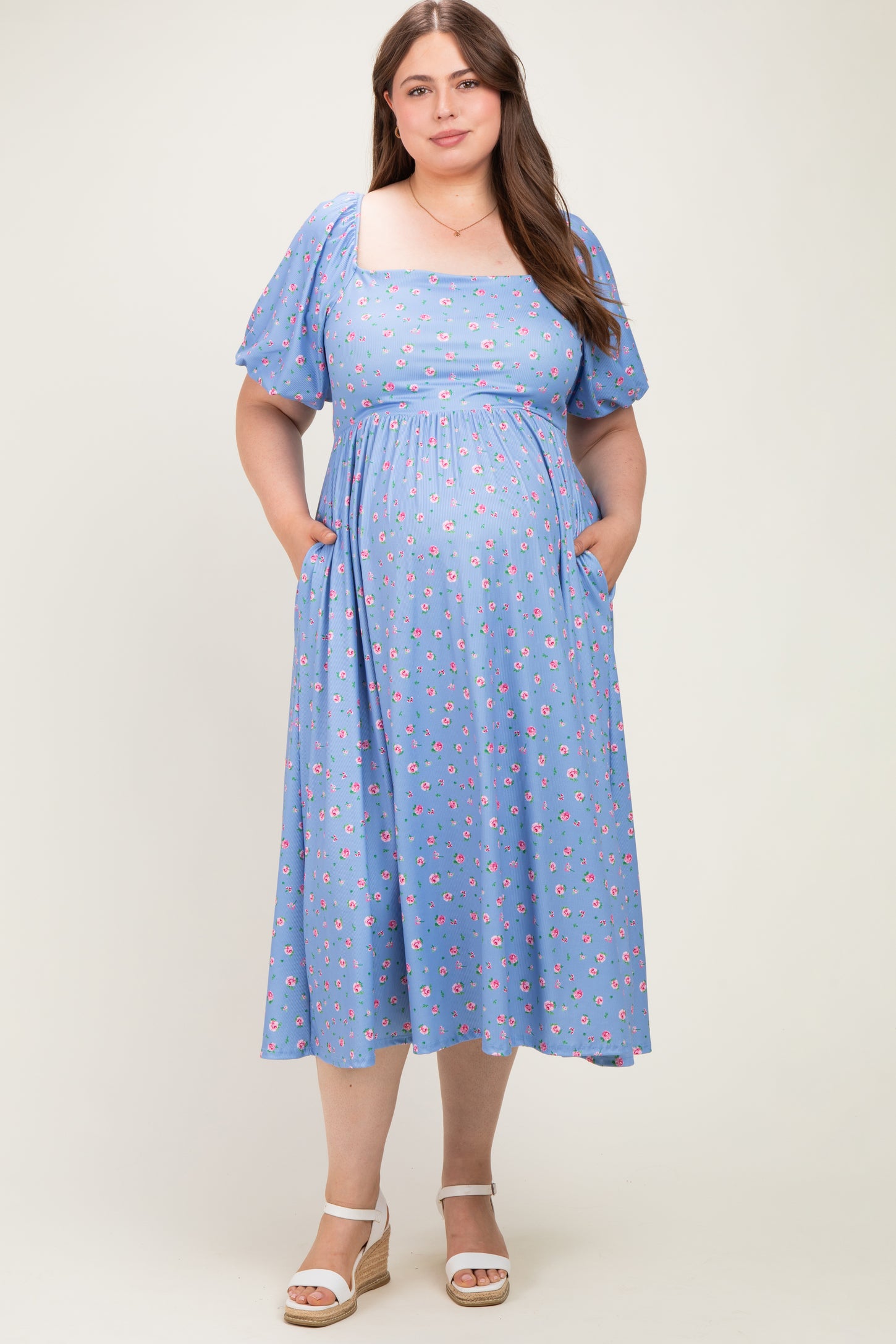 woman wearing a light blue floral maternity dress with puff sleeves and pockets, showcasing her baby bump