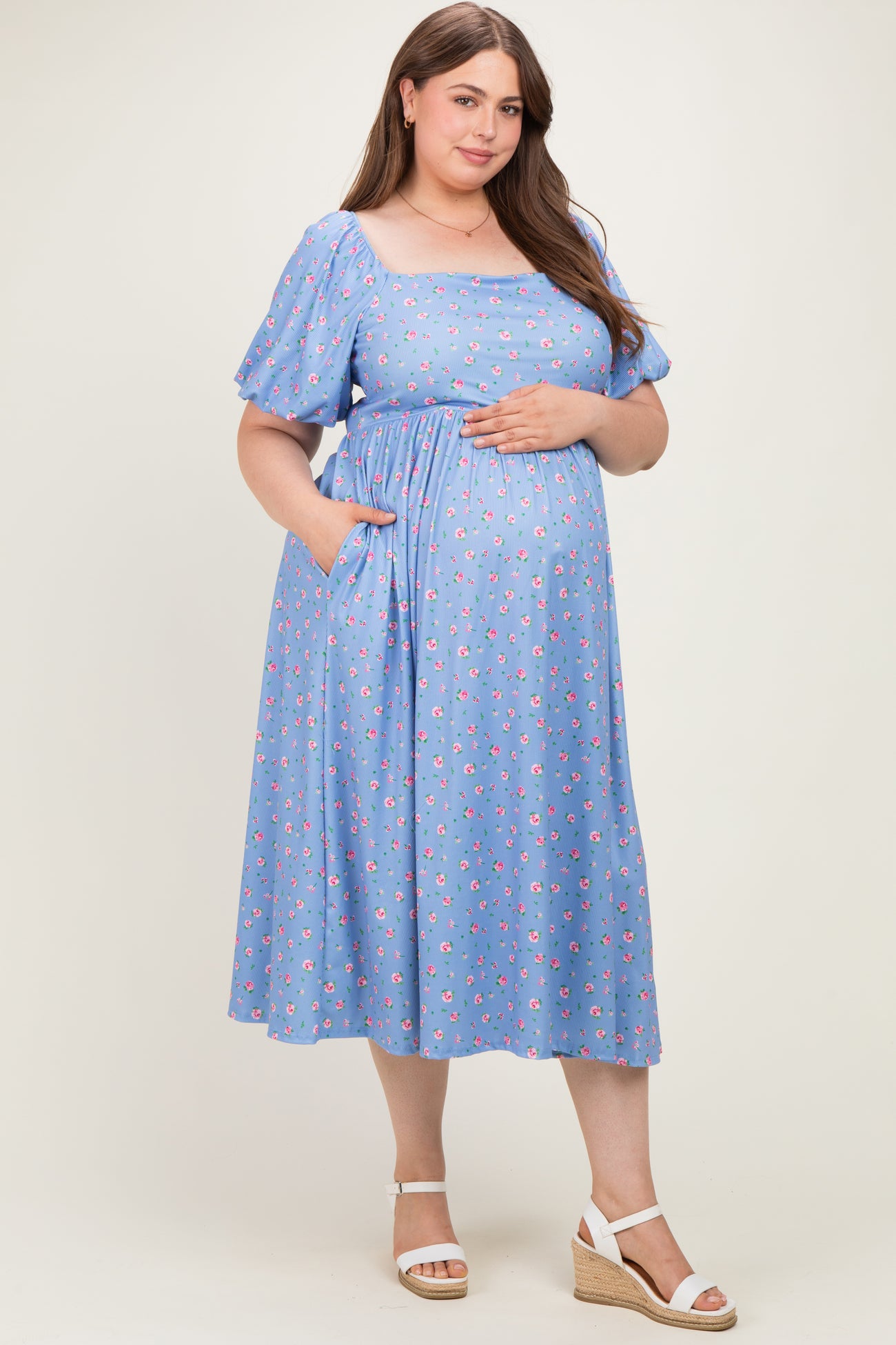 woman wearing a light blue maternity dress with floral print, short puff sleeves, and pockets, showing her baby bump