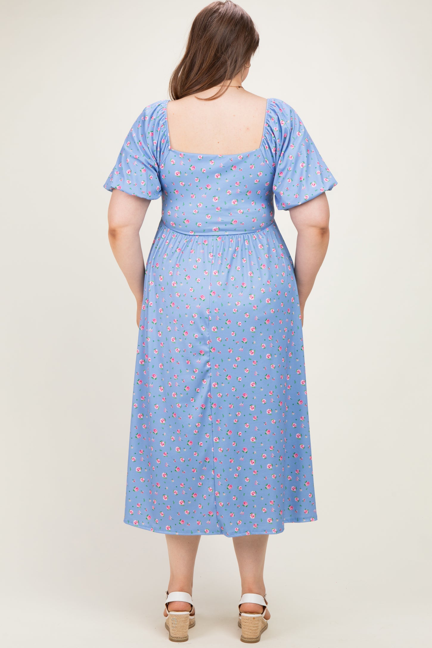 woman wearing a blue floral print maternity dress with short puff sleeves and an elasticated waist, showing her baby bump