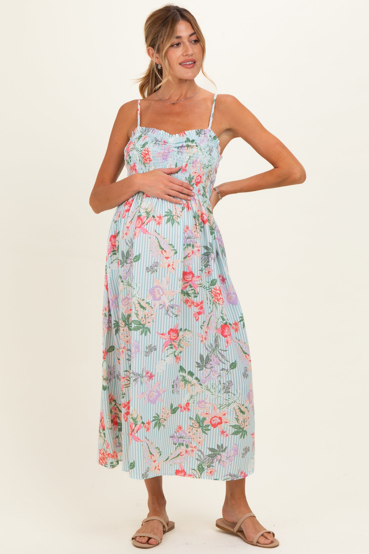 woman wearing a light blue floral maternity maxi dress with smocking and adjustable straps, showcasing her baby bump