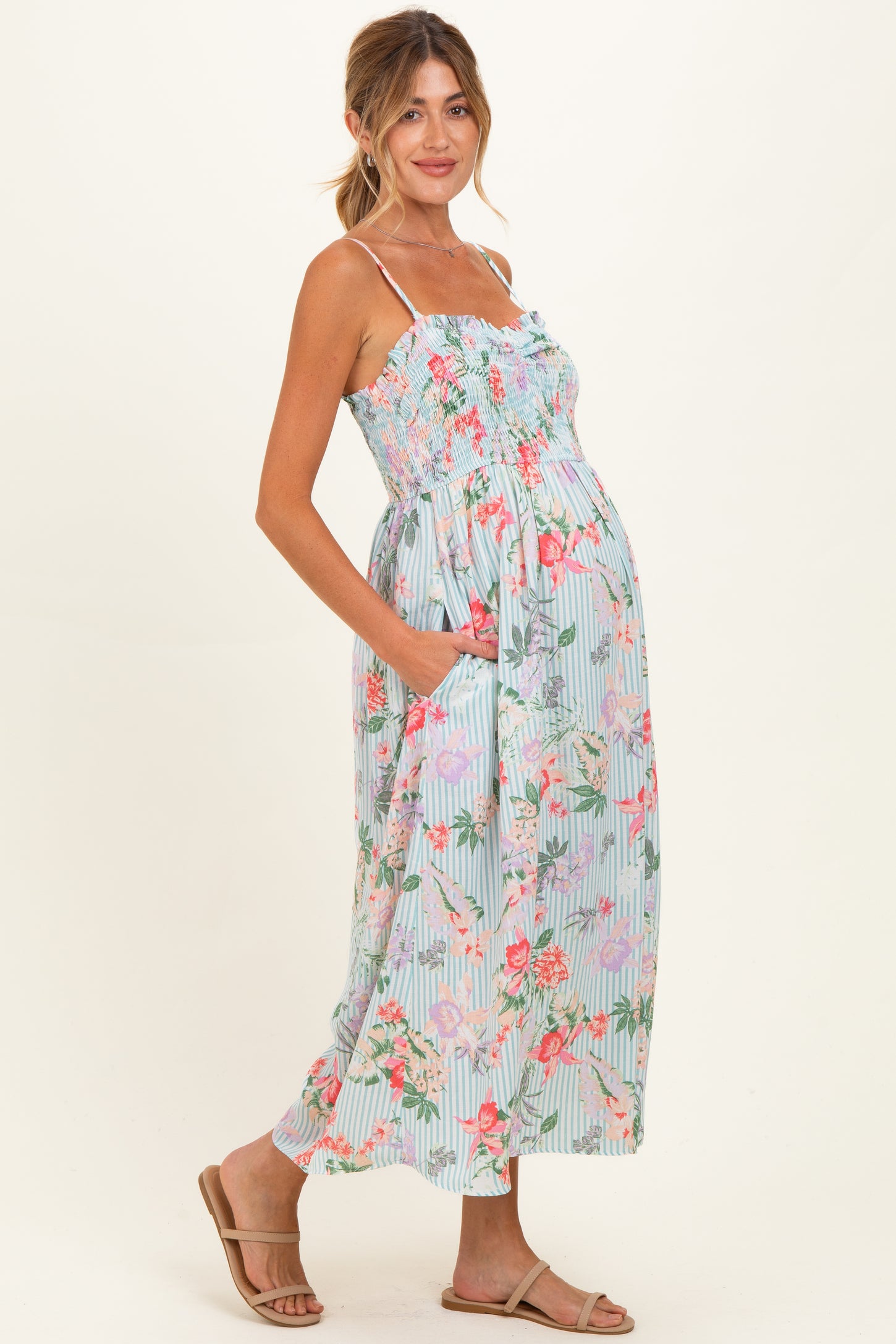 woman wearing a floral patterned maternity maxi dress with adjustable straps and pockets, showcasing her baby bump