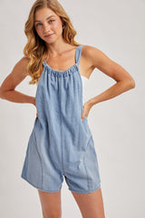 woman wearing a light blue denim overall romper with adjustable straps and a relaxed fit