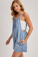 woman wearing a light blue denim overall dress with pockets and a gathered neckline, styled over a white top