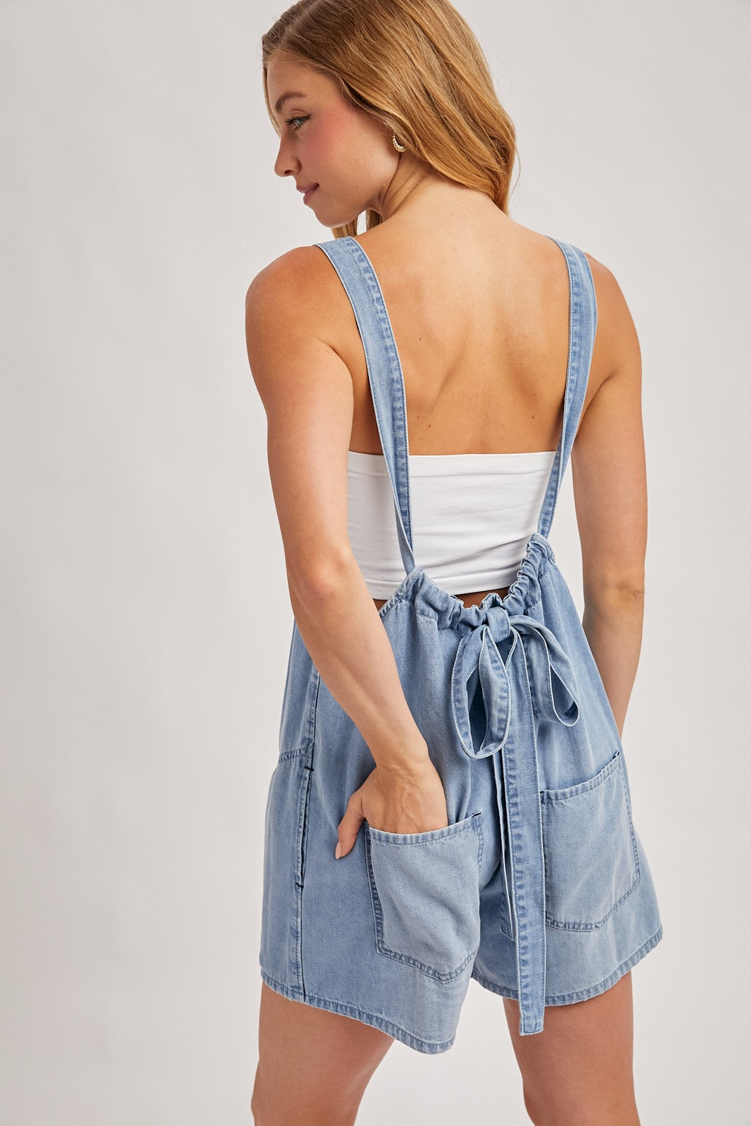 woman wearing a light blue denim romper with adjustable straps and two front pockets