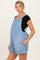 woman wearing a light blue maternity denim overall dress with pockets and adjustable straps, showing her baby bump