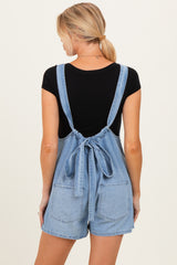 woman wearing a light blue maternity denim overall romper with adjustable tie straps and back pockets