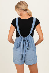 woman wearing a black short sleeve top and a light blue denim maternity overall with tie-back detail and pockets