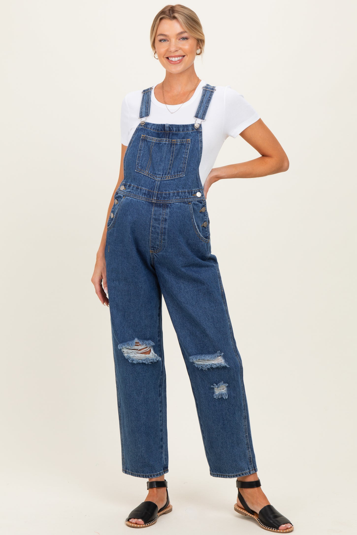 woman wearing a maternity denim overall with distressed details and a white t-shirt, showcasing her baby bump