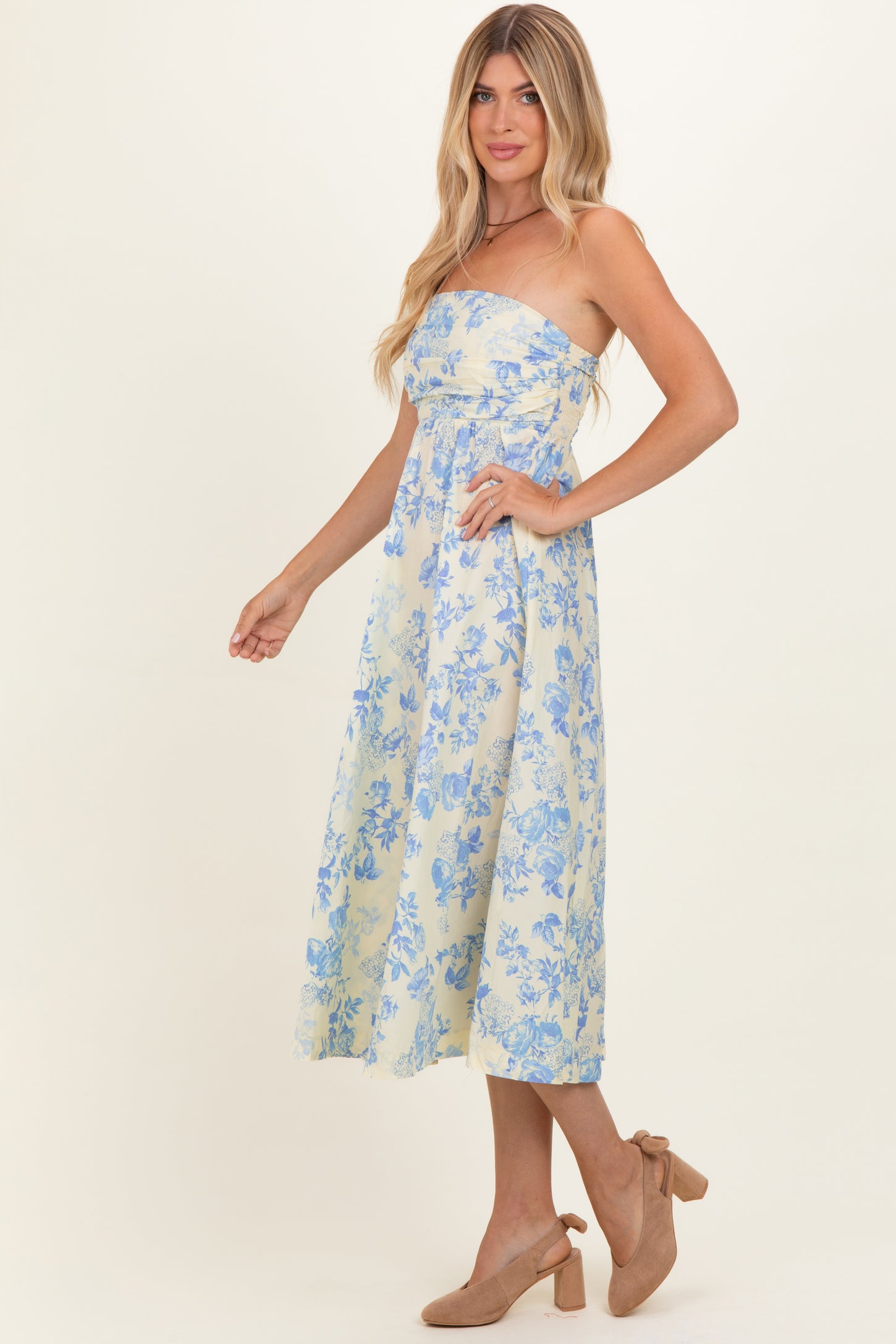 woman wearing a strapless yellow floral midi dress with blue patterns and beige heels