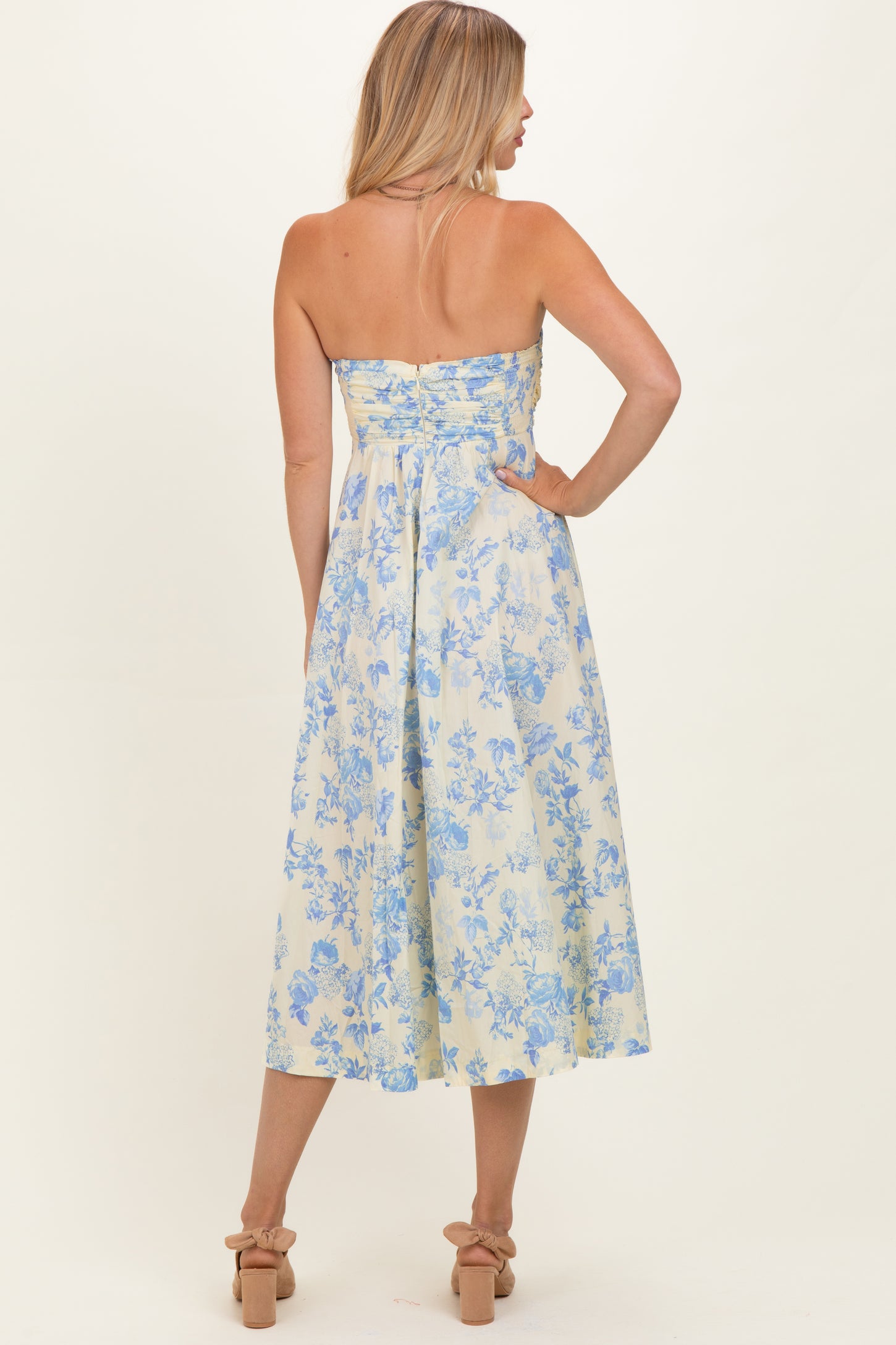 woman wearing a strapless floral midi dress in light blue and yellow, showing the back view with a fitted bodice and flared skirt