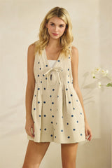 woman wearing a beige sleeveless romper with blue polka dots and a front tie detail