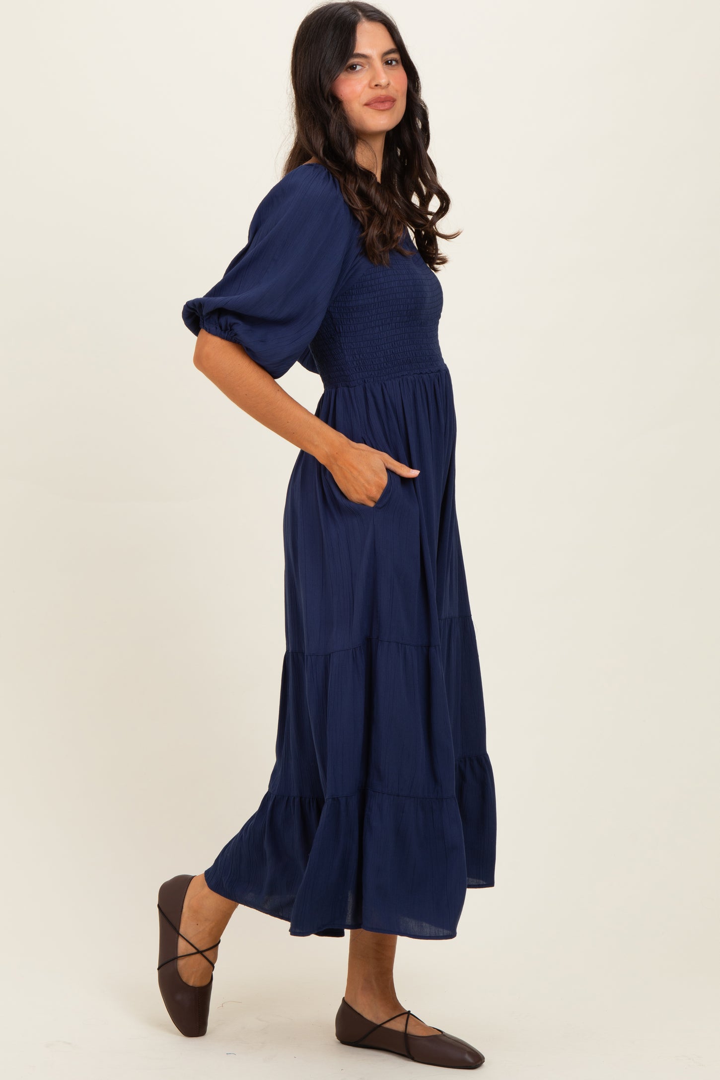 woman wearing a navy blue maxi dress with puff sleeves, smocked bodice, and tiered skirt, also has pockets