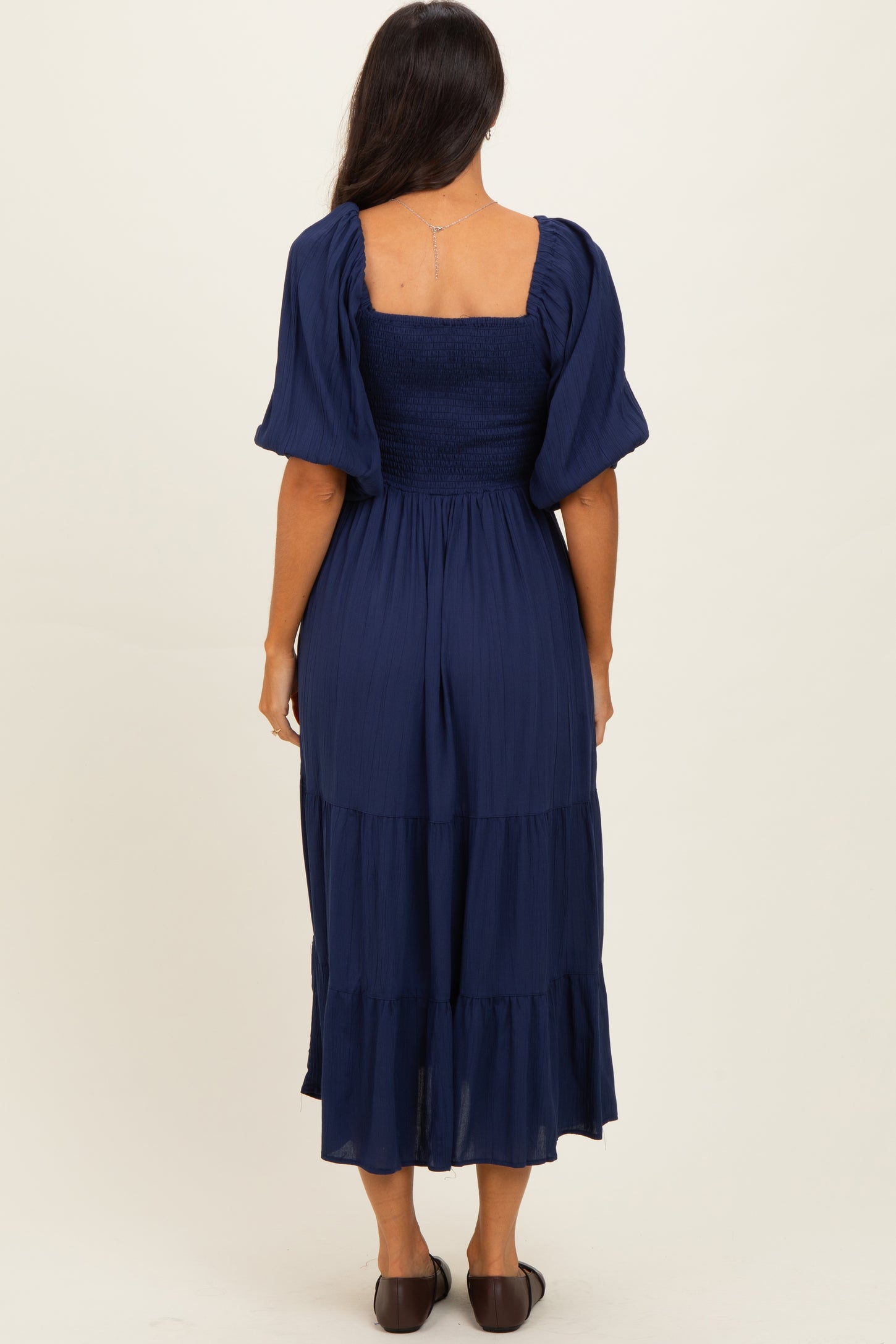 woman wearing a navy blue puff sleeve dress with a smocked bodice and tiered skirt, viewed from the back