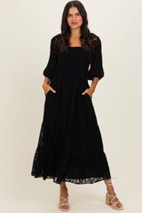 woman wearing a black lace maxi dress with smocked bodice and puff sleeves, standing with pockets visible