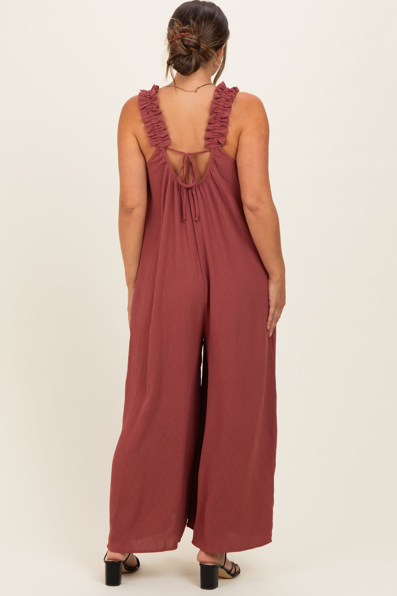 woman wearing a rust-colored maternity jumpsuit with ruffled straps and an open back