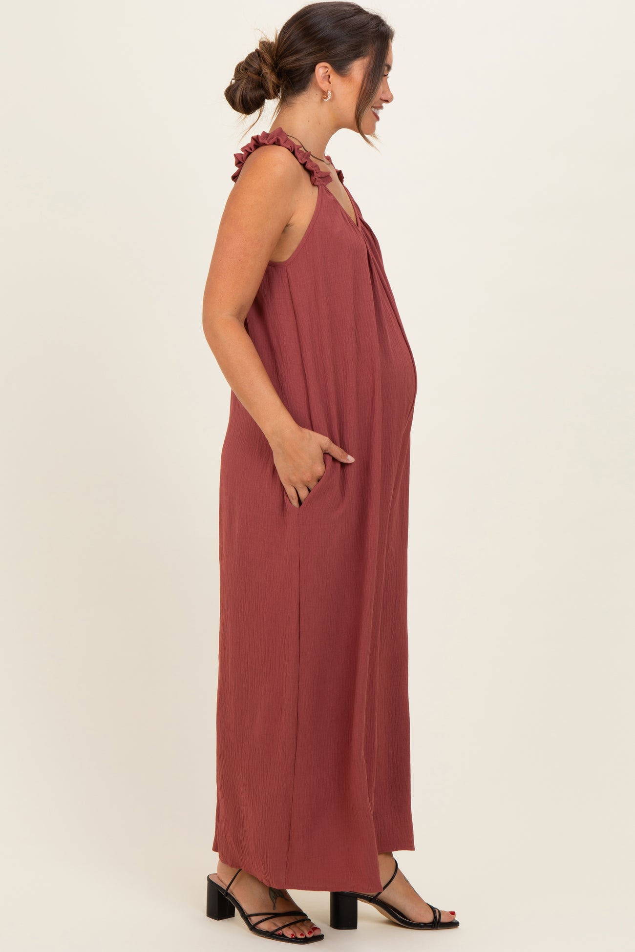 woman wearing a rust-colored maternity maxi dress with ruffled straps and side pockets, showcasing her baby bump