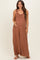 woman wearing a rust-colored maternity jumpsuit with ruffled straps and a visible baby bump