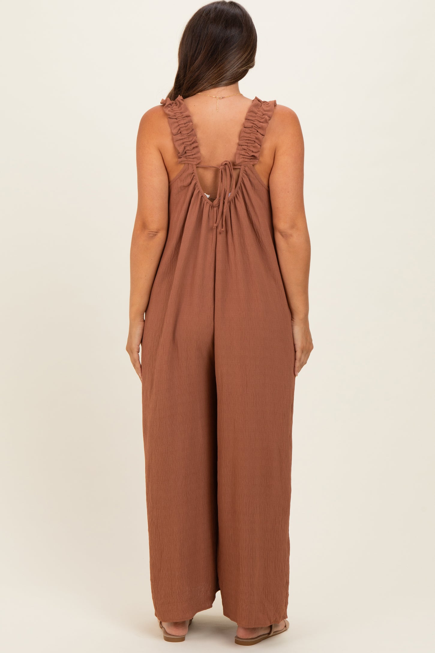 woman wearing a brown maternity jumpsuit with ruffled straps and an open back