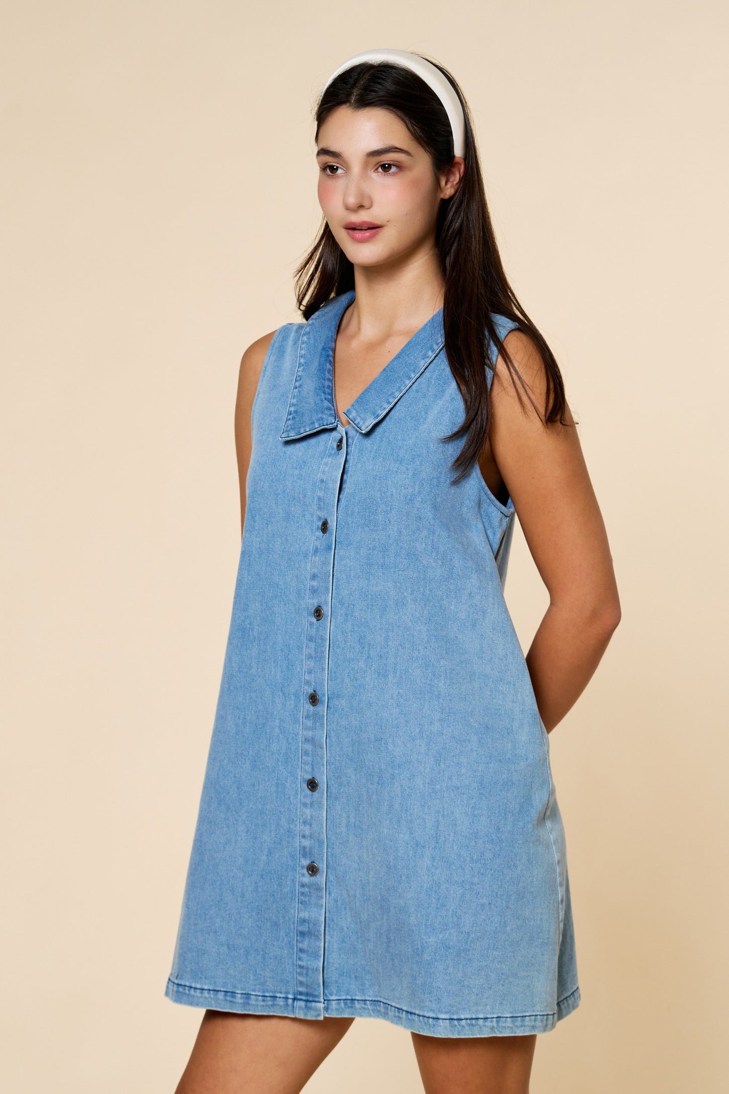 woman wearing a light blue denim sleeveless dress with a collar and button-down front