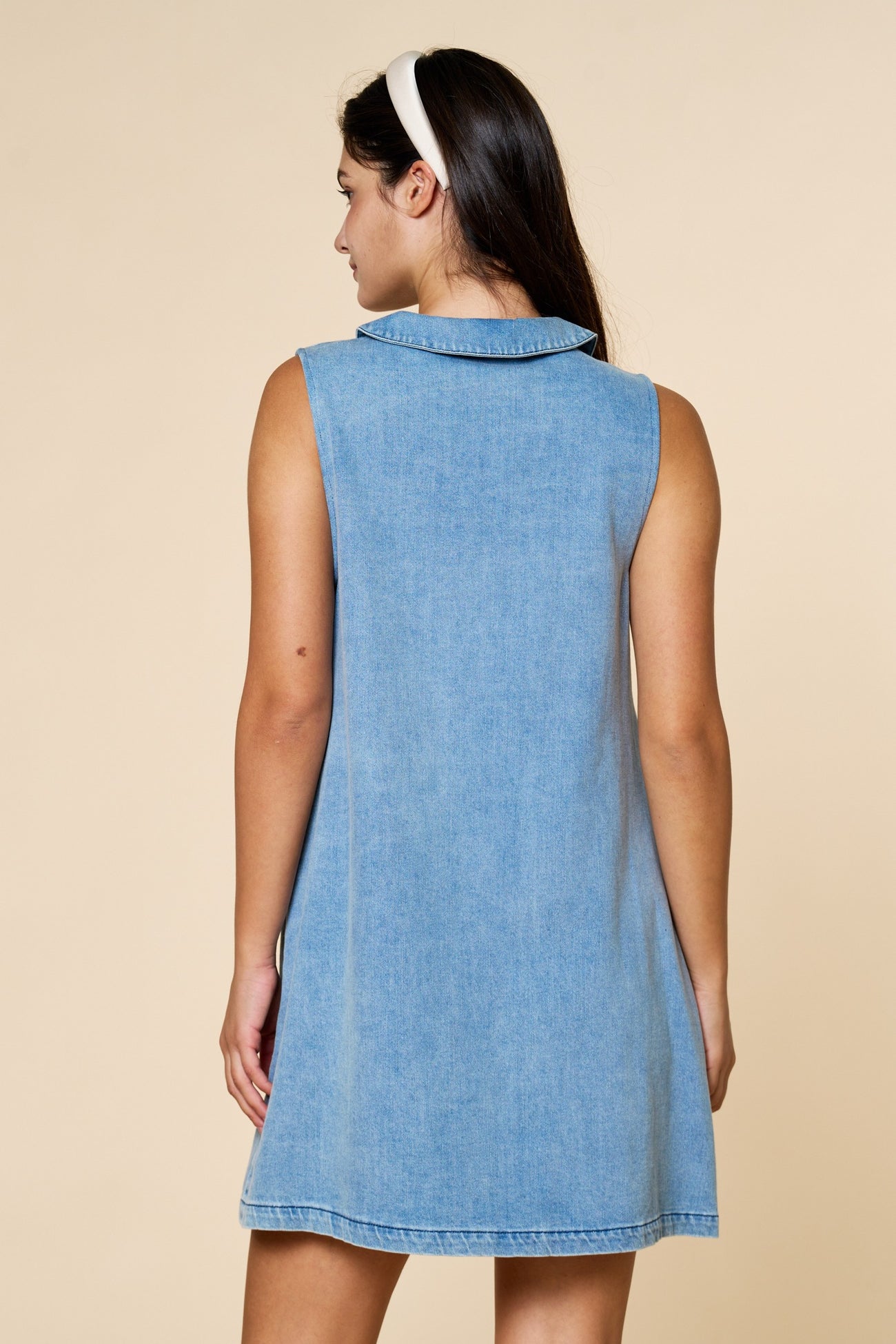 woman wearing a sleeveless light blue denim dress with a collar, shown from the back