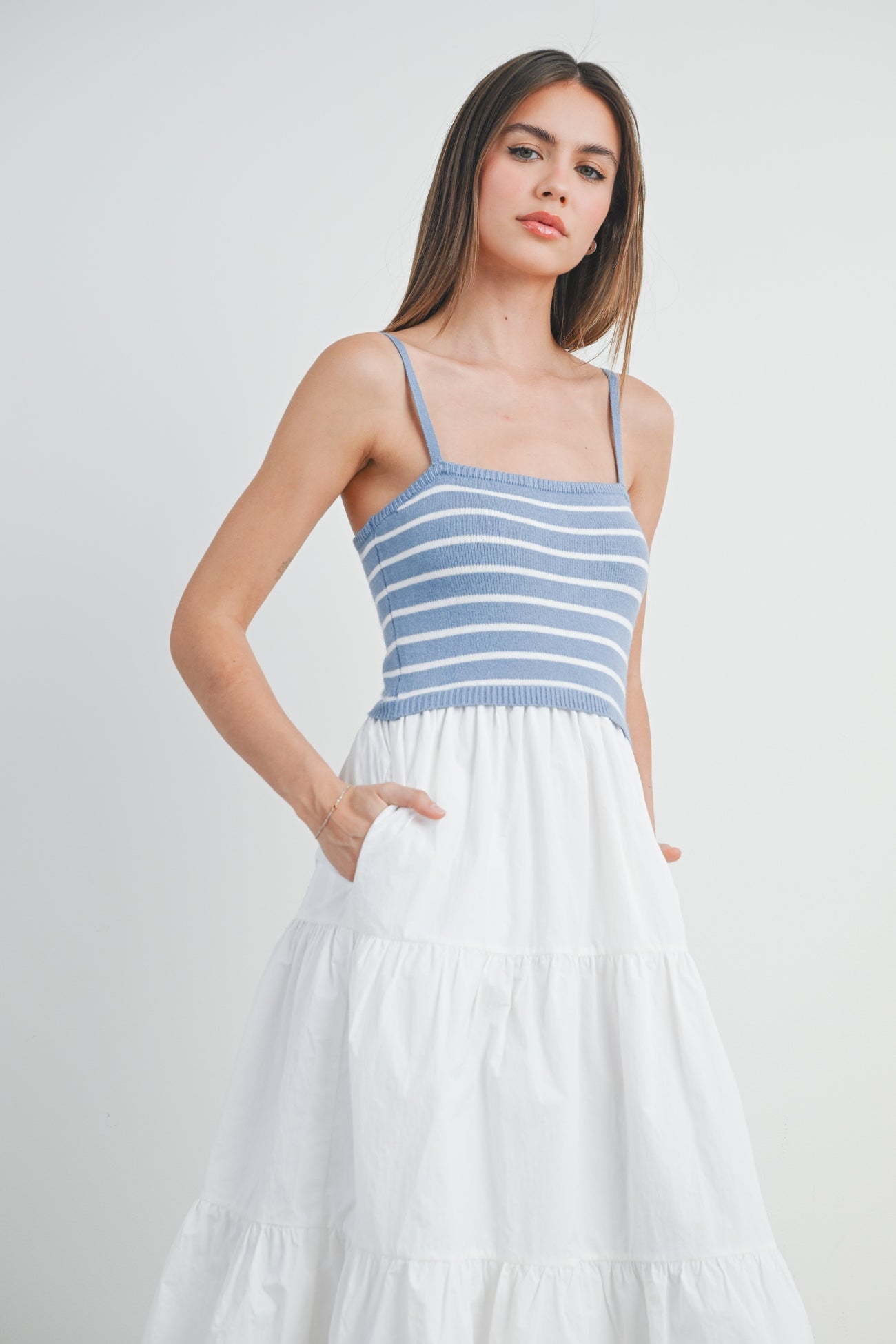 woman wearing a blue and white striped sundress with a fitted top and a flowy white tiered skirt, pockets visible