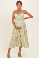 woman wearing a light yellow floral print maternity dress and holding her baby bump
