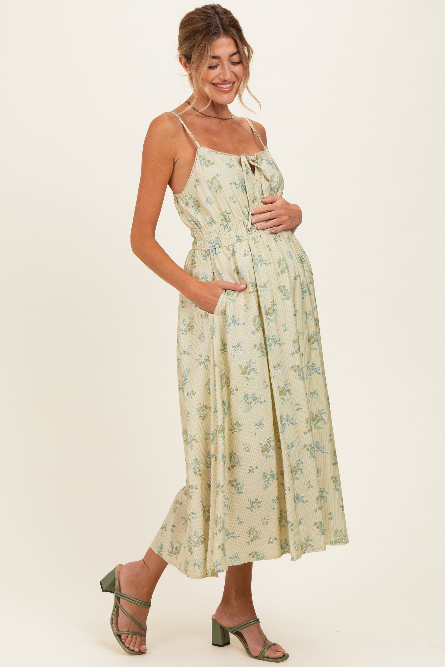 woman wearing a floral print yellow maternity dress with adjustable straps and pockets, highlighting her baby bump