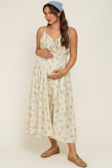 woman wearing a cream floral maternity dress with adjustable straps and a gathered waist, holding her baby bump