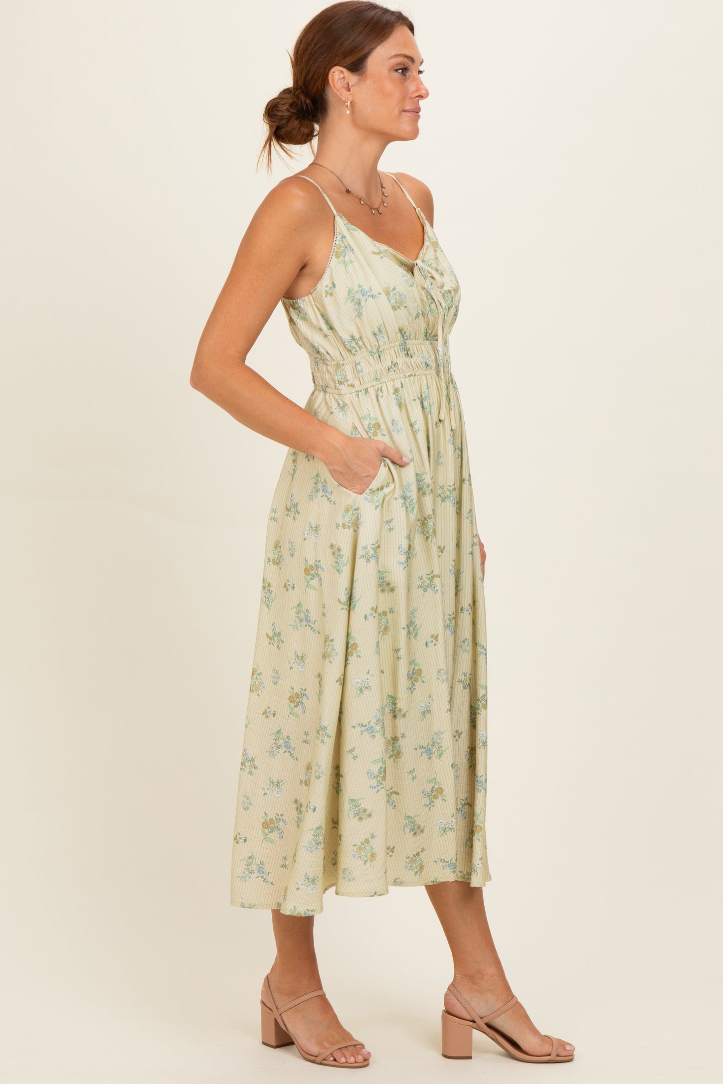 woman wearing a light yellow floral midi dress with a cinched waist and pockets, standing in profile