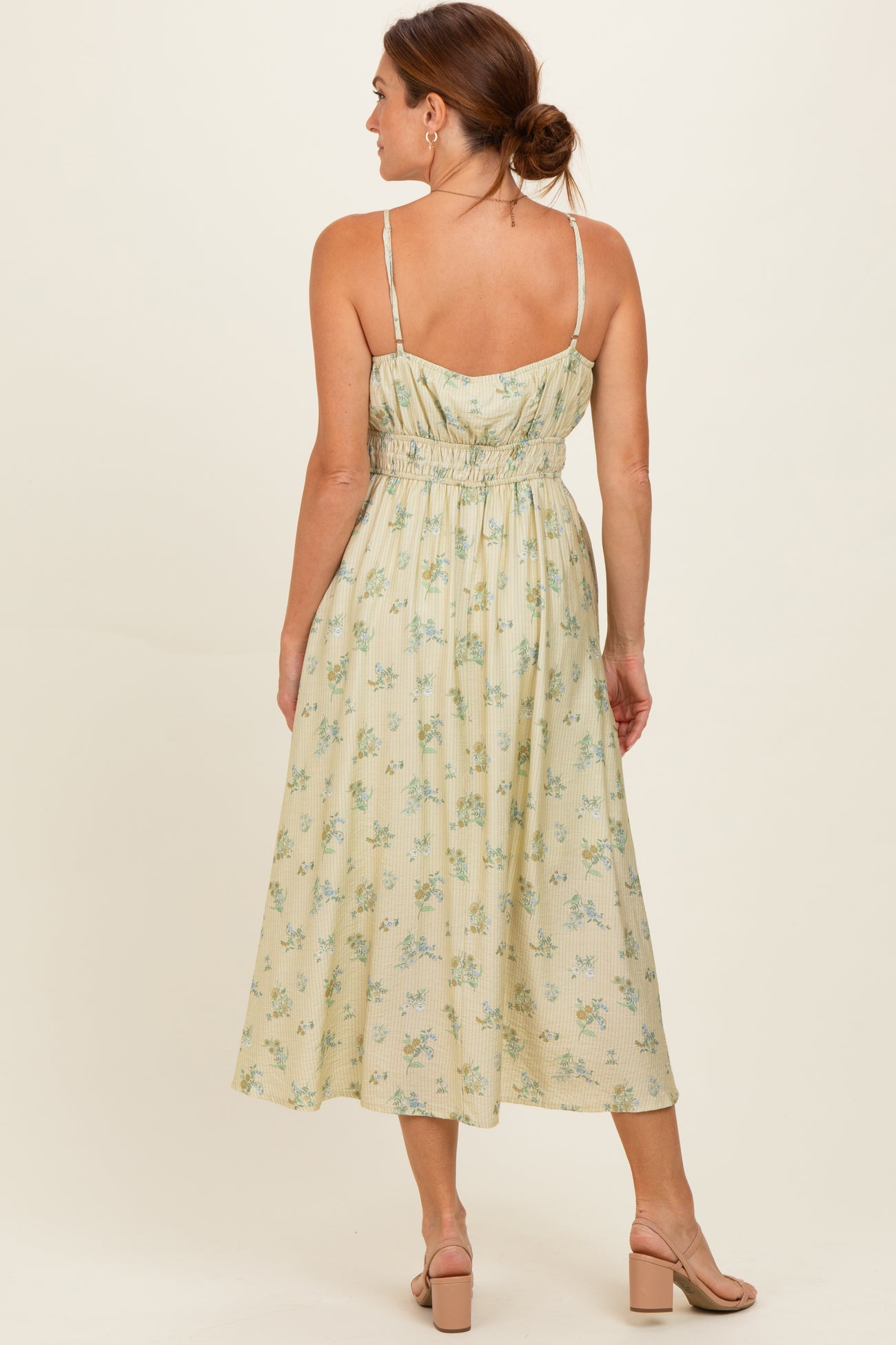 woman wearing a light yellow floral midi dress with a smocked back and thin straps, shown from the back