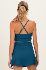 woman wearing a teal maternity sports bra with crisscross straps and a matching skort