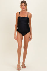 woman wearing a black maternity swimsuit with gathered detailing and adjustable straps, showcasing a baby bump