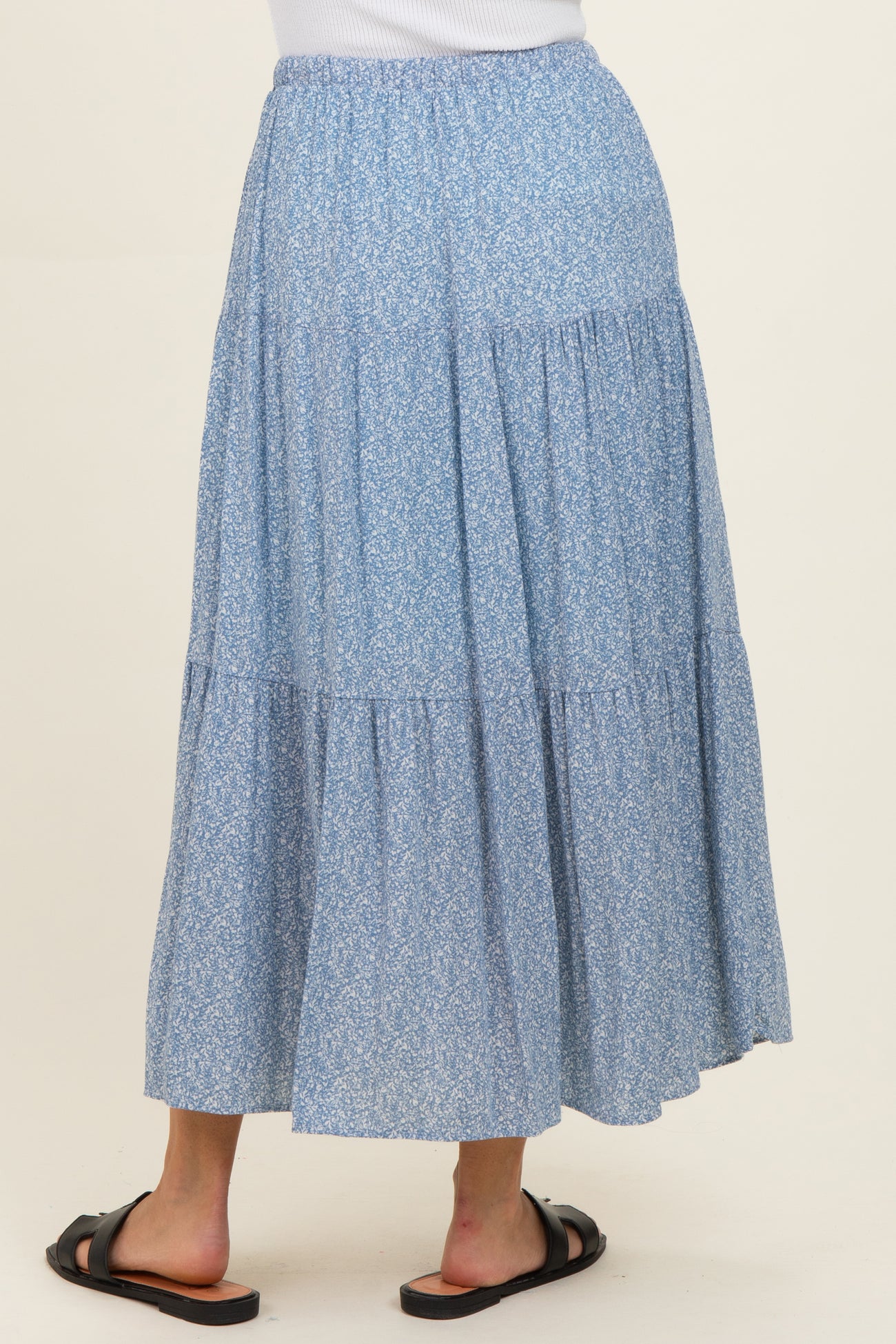 woman wearing a flowy blue floral maxi skirt with a tiered design and elastic waistband, viewed from the back