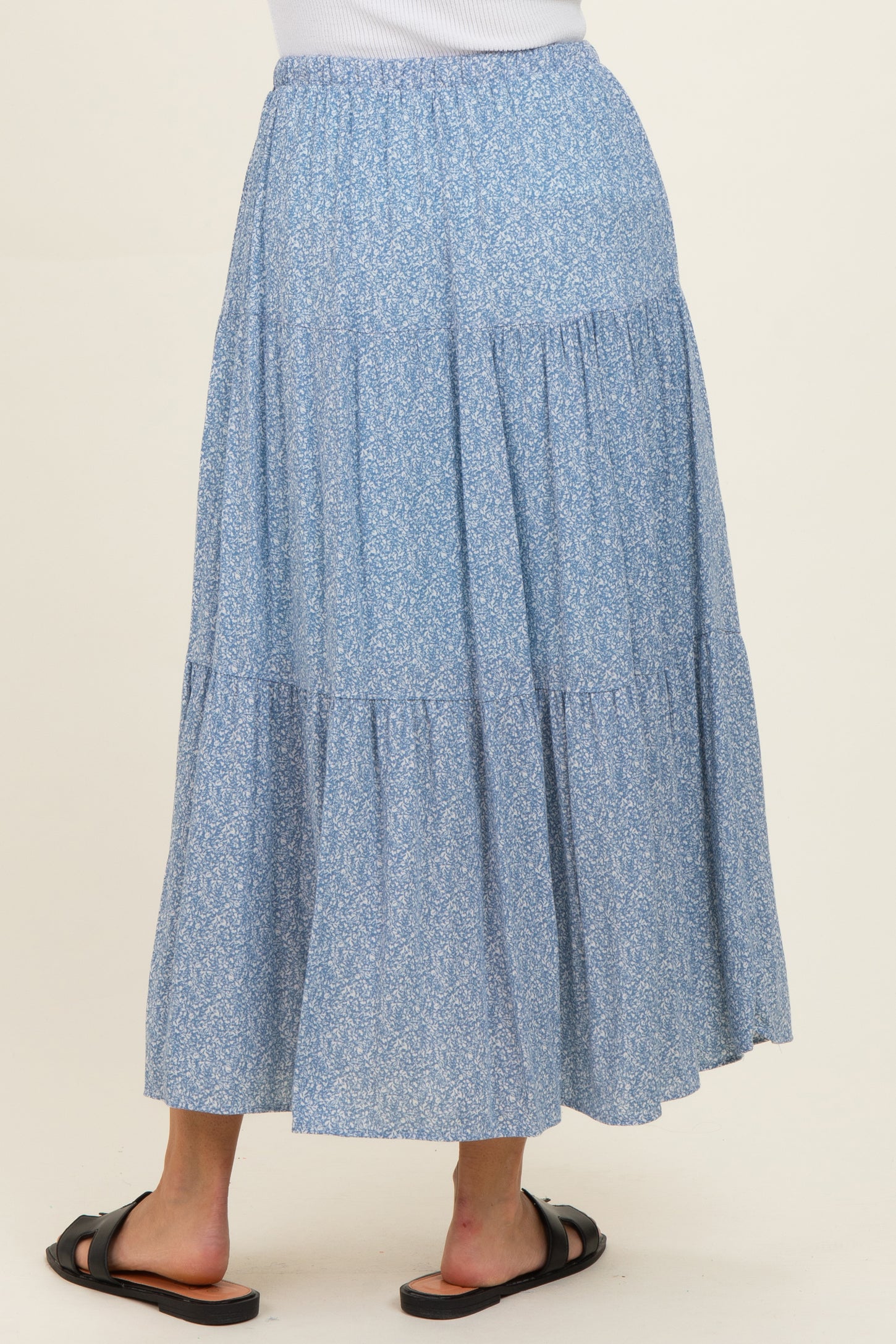 woman wearing a flowy blue floral maxi skirt with a tiered design and elastic waistband, viewed from the back