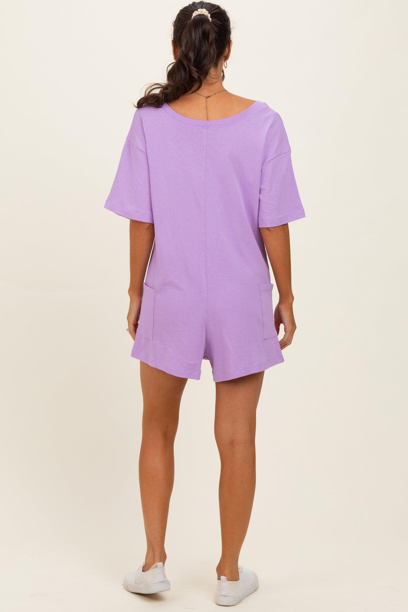 woman wearing a lavender short sleeve romper with pockets, viewed from the back