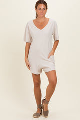 woman wearing a light beige short sleeve romper with a v-neck and side pockets