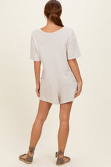 woman wearing a light beige short sleeve romper with a relaxed fit and side pockets, view from the back