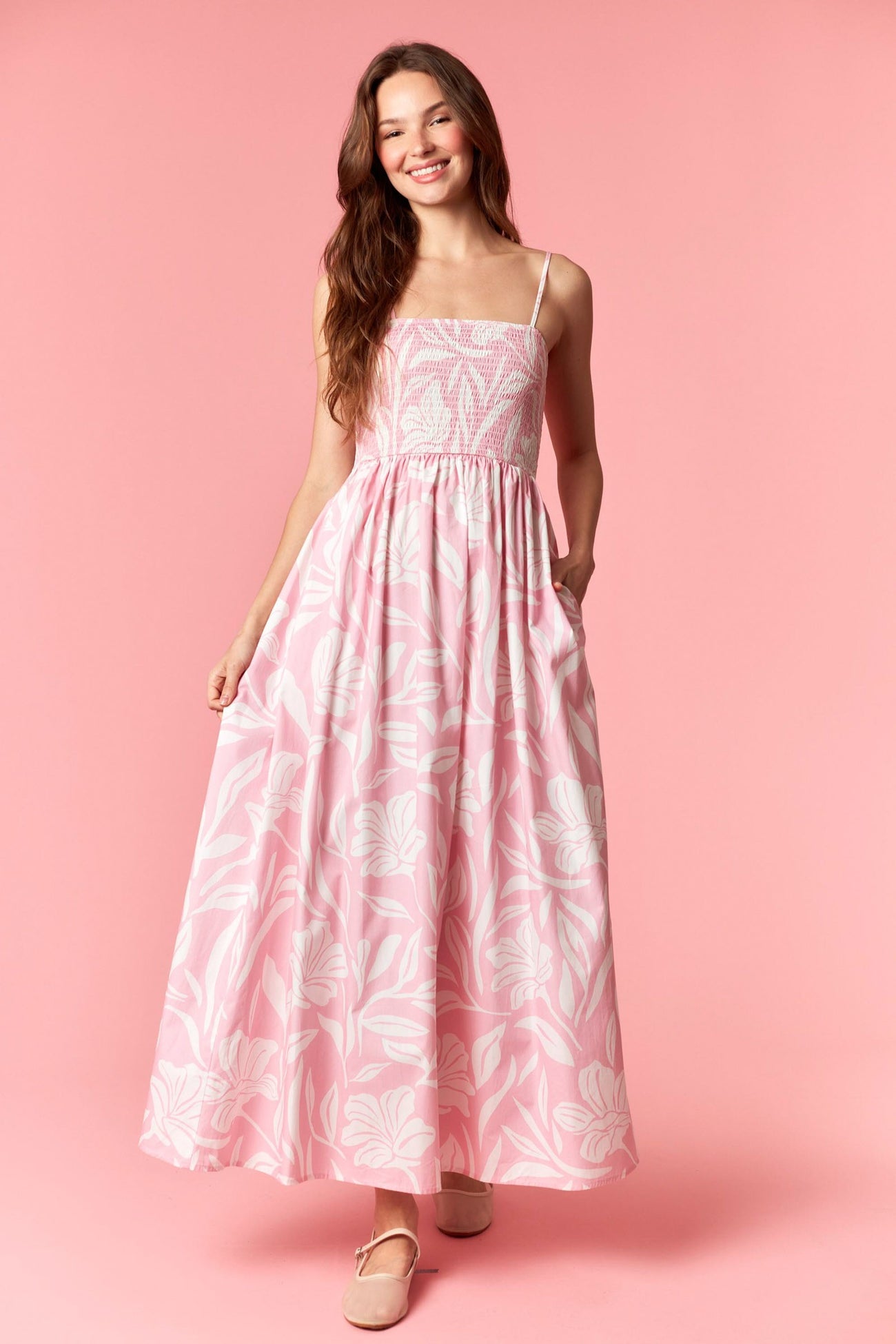 woman wearing a pink floral maxi dress with adjustable spaghetti straps and pockets