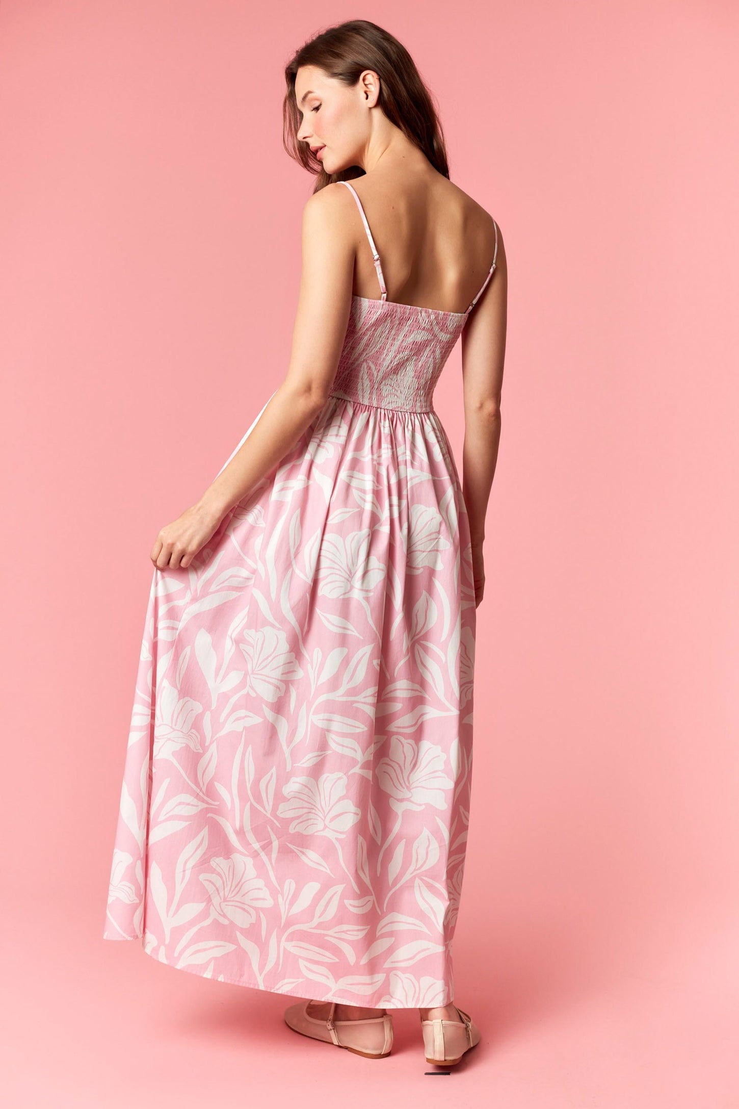 woman wearing a pink floral maxi dress with thin straps, showing the back and flowing skirt
