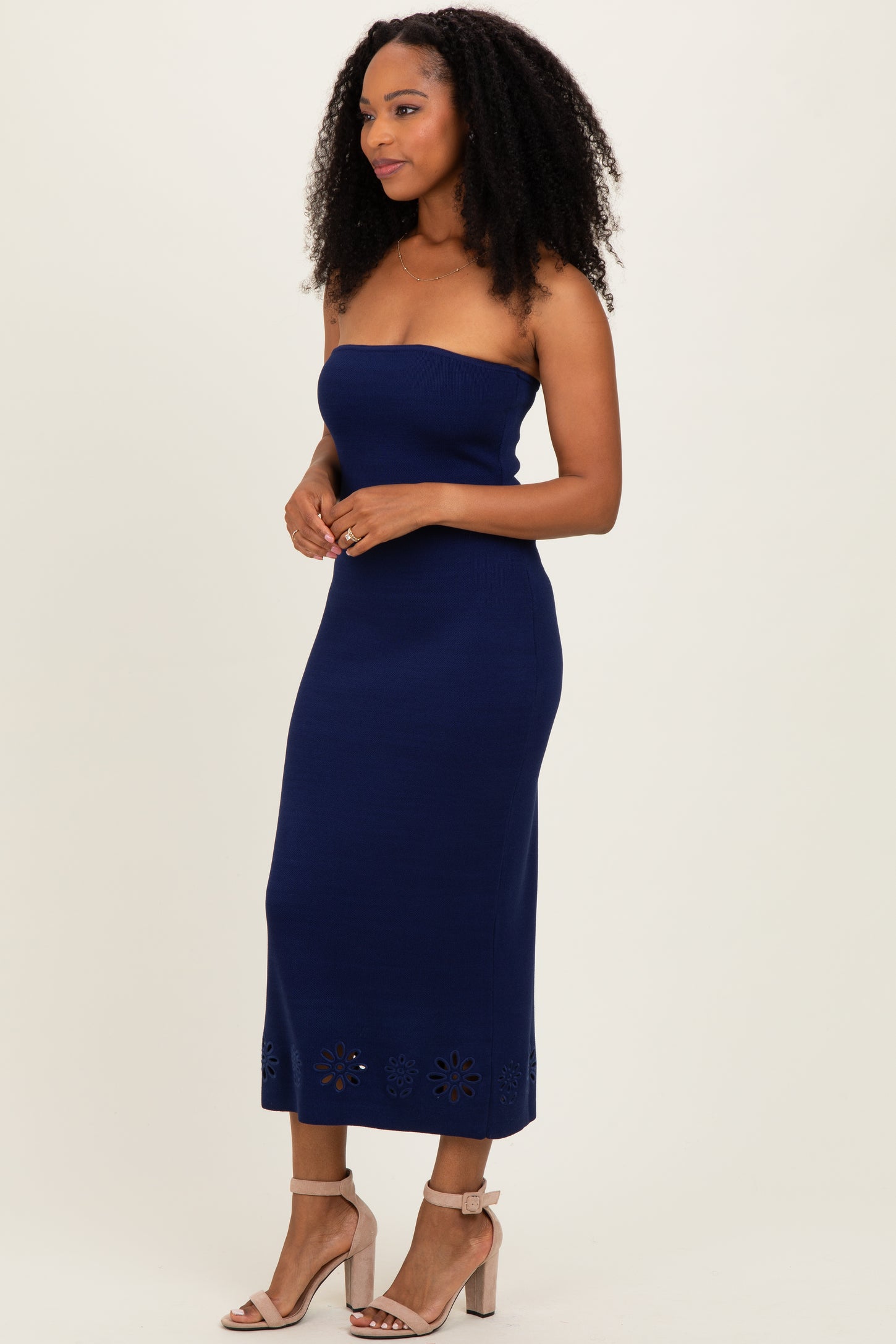 woman wearing a navy strapless midi dress with embroidered floral details at the hem and nude high-heeled sandals