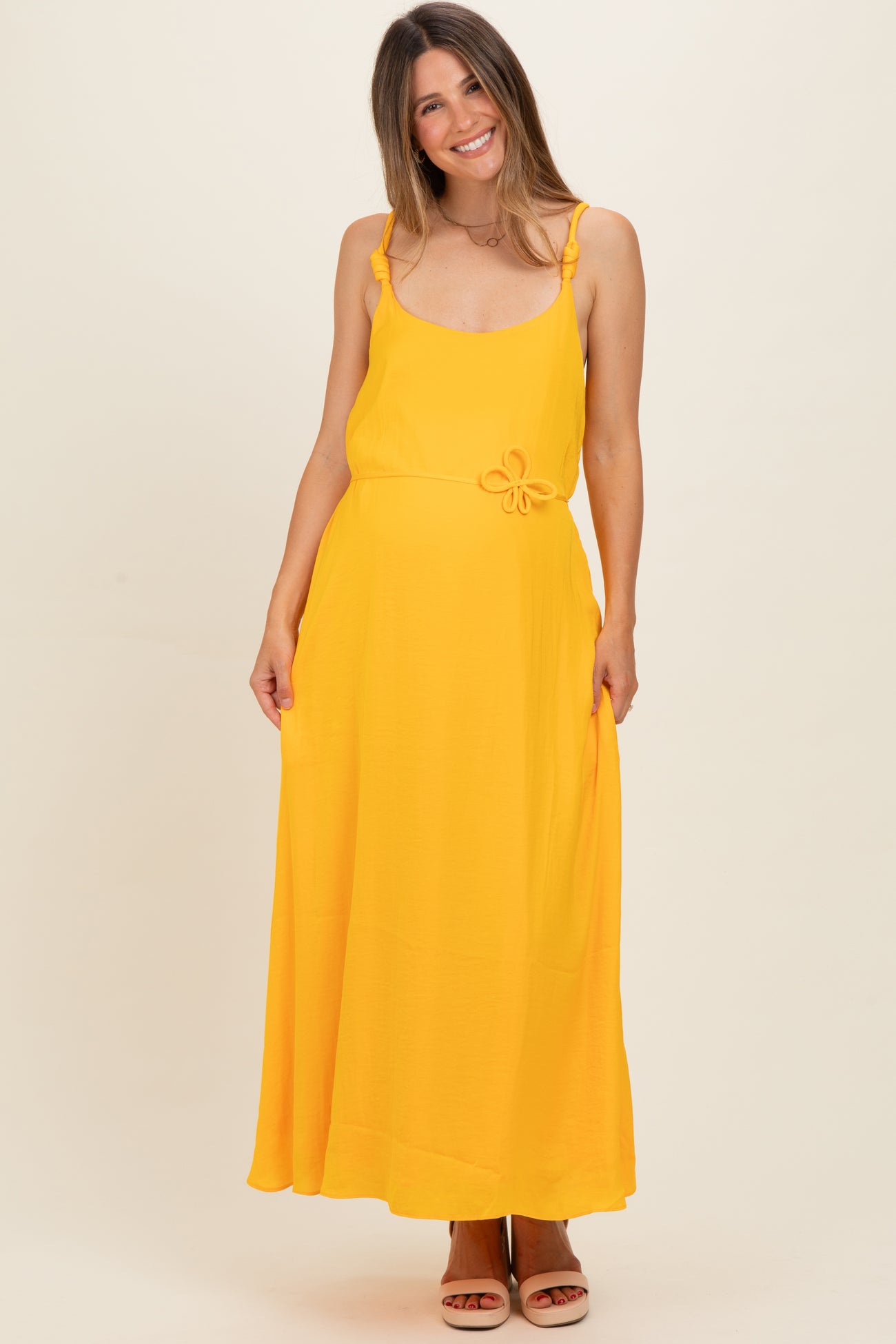 woman wearing a bright yellow maternity maxi dress with ruffle straps and a bow detail at the waist